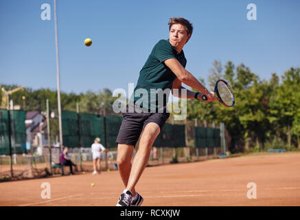 Un uomo giocando a tennis sulla corte su una bella giornata di sole Foto Stock