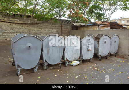 Vuoto grigio grandi contenitori per rifiuti in una fila su un soleggiato strada urbana. Una fila di ferro grigio bidoni della spazzatura in strada - Immagine Foto Stock