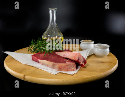 Due entrecote bistecca su un tagliere di legno con olio di oliva Rosmarino sale e pepe pronti per la cottura Foto Stock