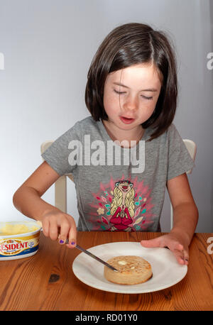 Ragazza giovane buttering un crumpet tostato Foto Stock