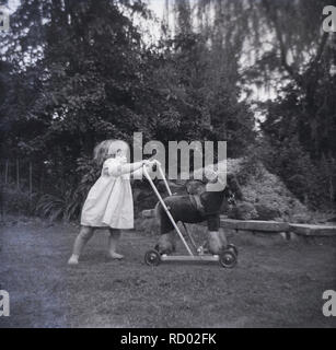 Degli anni Cinquanta, storico, infantile ragazza in scalza fuori in un giardino sul retro spingendo un cavallo giocattolo su ruote, Inghilterra, Regno Unito. Foto Stock