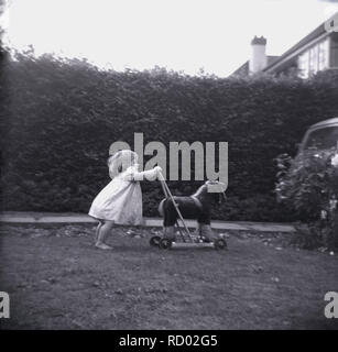 Degli anni Cinquanta, storico, infantile ragazza in scalza fuori in un giardino frontale spingendo un cavallo giocattolo su ruote, Inghilterra, Regno Unito. Foto Stock