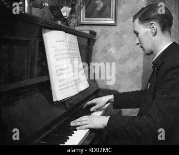 Degli anni Cinquanta, storico, a casa di un uomo in una tuta la riproduzione di ''La corda perduto" su un pianoforte, England, Regno Unito Foto Stock