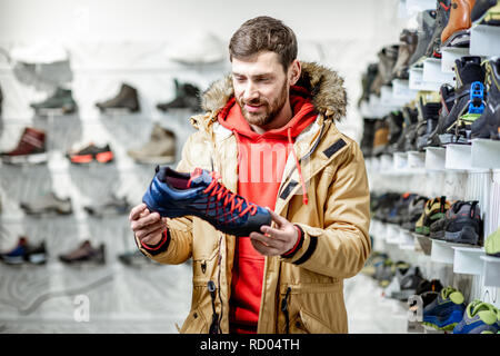 Uomo in giacca invernale Scegliendo trail scarpe da trekking in montagna nel negozio di articoli sportivi Foto Stock