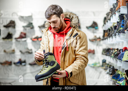 Uomo in giacca invernale Scegliendo trail scarpe da trekking in montagna nel negozio di articoli sportivi Foto Stock