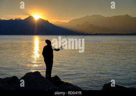 Fisherman silhouette contro l'oceano, con tramonto sulla montagna in background. Foto Stock