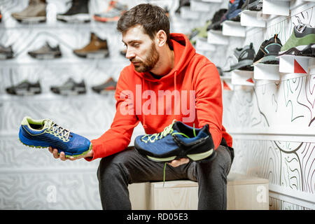 L'uomo scegliendo trail scarpe da escursionismo seduti nella sala di montaggio dei moderni sport shop Foto Stock