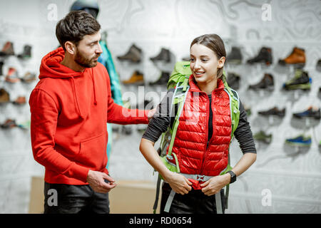 Rappresentante di vendita attrezzature di viaggio di una giovane donna di client che cerca uno zaino nel negozio di articoli sportivi Foto Stock