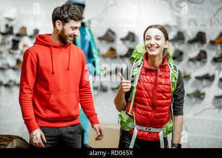 Rappresentante di vendita attrezzature di viaggio di una giovane donna di client che cerca uno zaino nel negozio di articoli sportivi Foto Stock