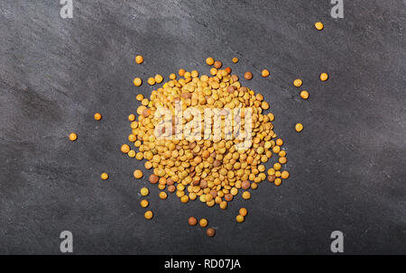 Materie lenticchie sulla pietra nera dello sfondo. Una sana alimentazione vegetariana concetto. Superfoods. Vista superiore, copia dello spazio. Le lenticchie sono ricche di carboidrati complessi, f Foto Stock