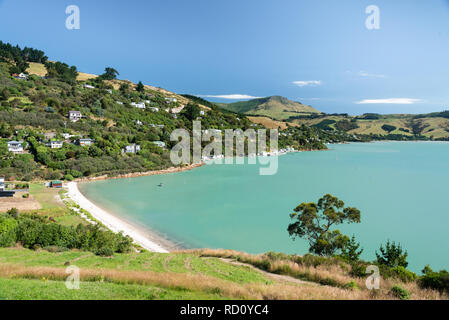 Le case punteggiano la collina che circonda le acque turchesi acquamarine di Hays Bay, Lyttelton Harbour, Banks Peninsula, South Island, Nuova Zelanda Foto Stock