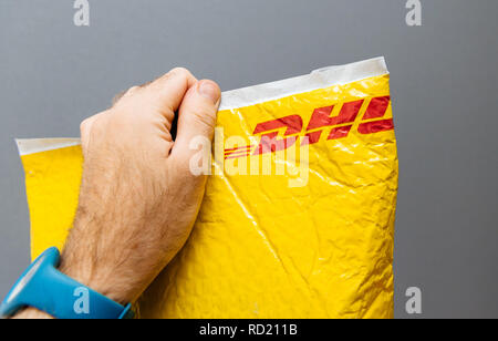 Parigi, Francia - Mar 24, 2018: Maschio mano azienda contro uno sfondo grigio a DHL Express pacco giallo custodia in plastica Foto Stock