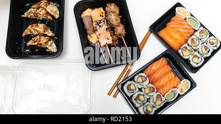 Vista da sopra della tabella contenente il sushi casella consegna con sushi california, Maki, sashimi, yakitori e bastoni di legno con wasabi e salsa di soia Foto Stock