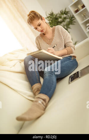 Bella giovane donna sorridente rilassante da disegno in un taccuino con matite colorate a casa. Foto Stock