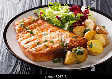 Grigliate di pesce spada bistecca guarnita con patate fritte e insalata fresca closeup alla piastra su una tavola di legno orizzontale. Foto Stock