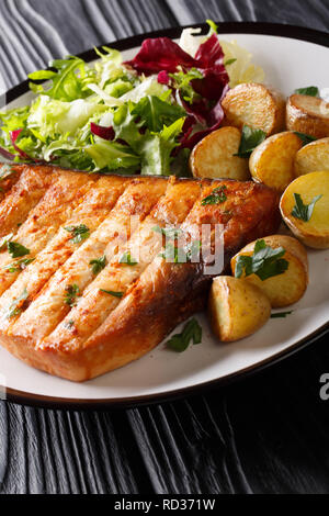 Pesce spada alla griglia di filetto con patate fritte e insalata fresca di close-up su una piastra su un tavolo di legno verticale. Foto Stock