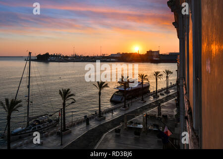 Il sole tramonta oltre il porto come dock barche lungo la passeggiata lungomare nella città costiera di Brindisi, Italia, nella regione Puglia Foto Stock