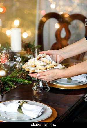 Donna mettendo un piatto di vaniglia crescent i cookie su un tavolo da pranzo di Natale Foto Stock