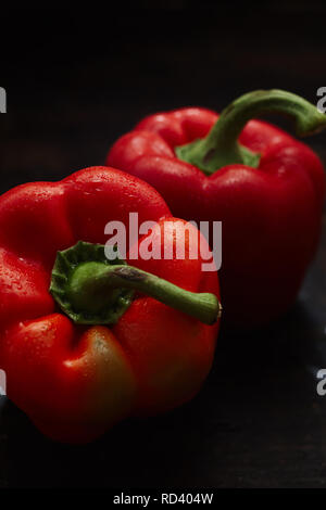 Due wet lavato crudo fresco di peperoni rossi o capsicum con gambi verdi per una insalata di sani ingredienti in un oscuro sfondo scuro visto elevato angolo Foto Stock