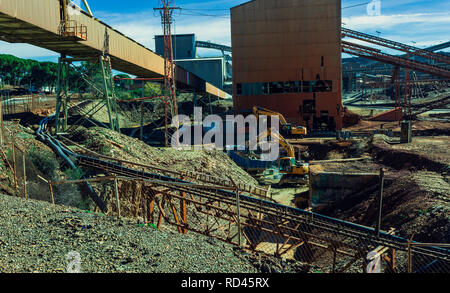 Ruota di retroescavatore del carico di un carrello di minerali e un altro escavatore nella ex miniera di Riotinto, con minerale di nastri trasportatori in background Foto Stock