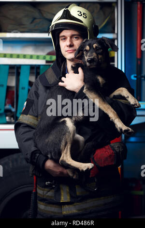 Immagine del giovane vigile del fuoco nel casco con il cane sullo sfondo del camion dei pompieri Foto Stock