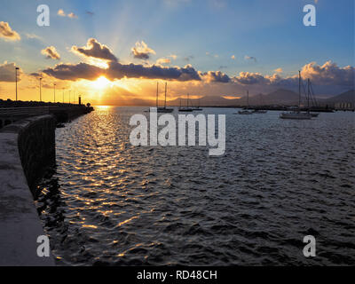 Bel tramonto con nuvole illuminato e pacifica barche a vela sull'oceano visto da una parete del mare a Arrecife, Lanzarote, Isole Canarie Foto Stock