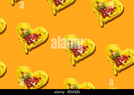 Duplicazione di decorativo cuore forme formata di giallo spaghetti con pomodoro e formaggio parmigiano topping, visualizzati in full frame da sopra Foto Stock