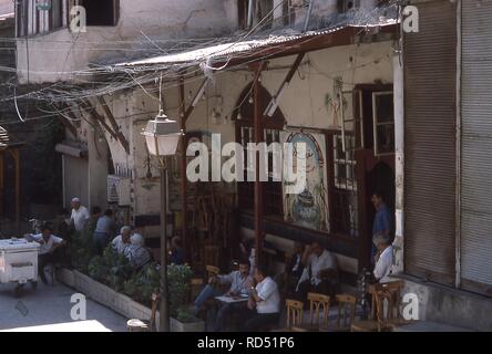 Scena di uomini rilassante su un patio ombreggiato al di fuori del Al-Nawfara Cafe situato dietro la Moschea degli omayyä di nella città vecchia di Damasco, Siria, Giugno 1994. La parete dipinta sign in arabo si traduce in "Al-Nawfara Cafe, Ahmad Sabah Ar-Ribat'. () Foto Stock