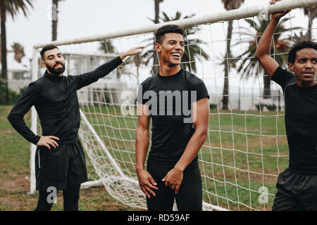 Tre i calciatori permanente al goalpost prendendo una pausa durante una partita di calcio. I giocatori di calcio facendo riscaldare in piedi vicino alla goalpost. Foto Stock
