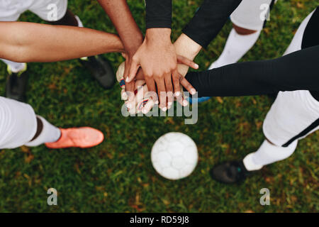 Vista dall'alto di mani di giocatori messi uno sopra l'altro in piedi in un huddle. I giocatori in piedi in un huddle unendo le loro mani assieme al centro w Foto Stock