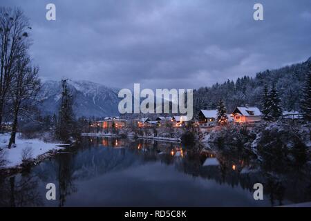 Piccole case coperte di neve e chtistmas luci nel pittoresco Bad Goisern, Hallstatt. Nightfall vista dal fiume. Foto Stock