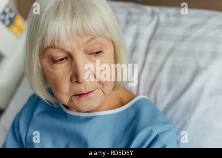 Triste senior donna con i capelli grigi che giace nel letto in ospedale Foto Stock