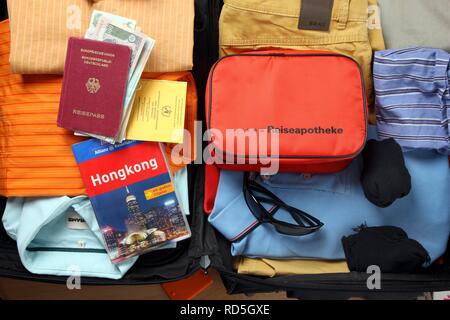 Holiday bagagli, kit di primo soccorso, passaporto, carta di vaccinazione, guida viaggi Foto Stock