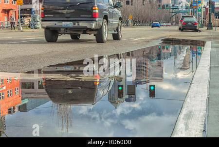 Riflessioni di un auto e gli edifici della città su una grande pozza di acqua piovana dopo una tempesta di neve nel centro di Seattle, Washington, Stati Uniti. Foto Stock