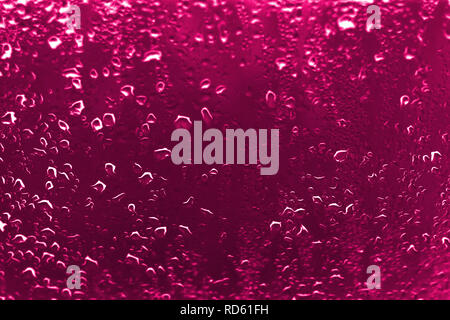 Alto contrasto foto di gocce di pioggia su un vetro di un finestrino con vivaci rossastro colore rosa Foto Stock