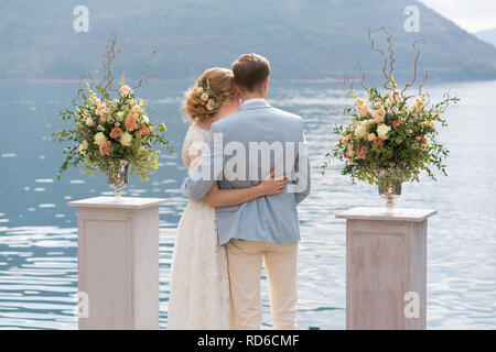 Sposa giovane sta abbracciando contro il mare tra le gabbie con composizioni floreali dopo la cerimonia di nozze Foto Stock