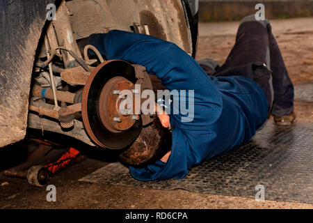 Un meccanico funziona giacente sul terreno di riparazione di una vecchia auto. Foto Stock