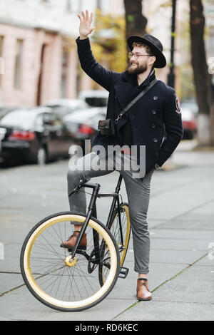 Casual bello hipster uomo Bicicletta Equitazione e salutando. Foto Stock