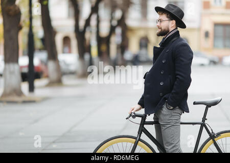 Bel uomo barbuto in bicchieri e trattenimento tappo bicicletta e sorridente Foto Stock