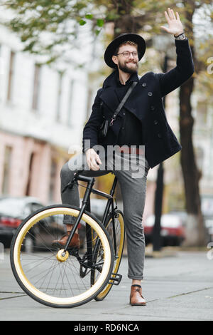 Casual bello hipster uomo Bicicletta Equitazione e salutando. Foto Stock