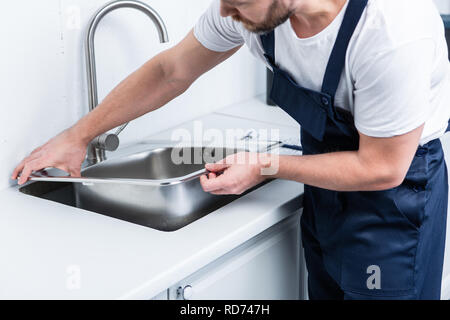 Vista parziale del barbuto repairman nel lavoro di fissaggio complessivo lavello in cucina Foto Stock