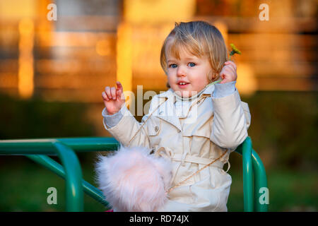 Ritratto di bionda sweet little Baby girl in trench coat e con fodera in pelliccia sintetica borsa a parco giochi Foto Stock