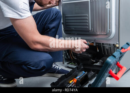 Vista parziale di aggiustatore nel lavoro complessivo refrigeratore di fissaggio con un cacciavite in cucina Foto Stock