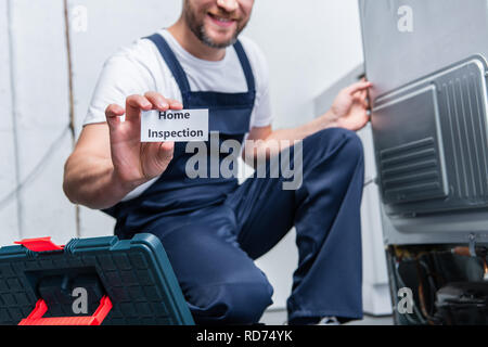 Vista parziale di adulto artigiano che mostra la scheda con scritte di ispezione iniziale mentre è seduto vicino al frigorifero rotto Foto Stock