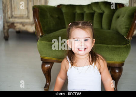 Ritratto di un felice ridere bambino ragazza seduta sul pavimento vicino alla sedia antica Foto Stock