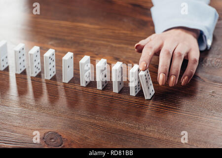 Vista ritagliata della donna spingendo domino fila sulla scrivania in legno con spazio di copia Foto Stock