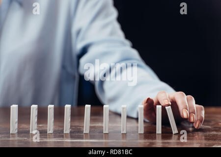 Vista ritagliata della donna spingendo domino fila sulla scrivania in legno Foto Stock