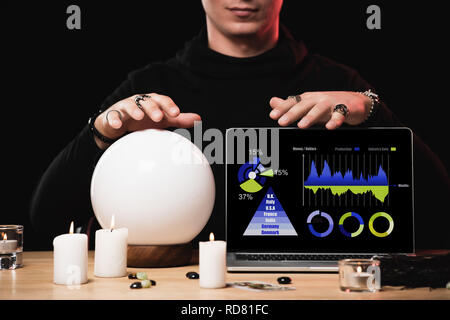 Vista ritagliata di esoterico nei pressi di laptop con tabelle e grafici sullo schermo isolato su nero Foto Stock