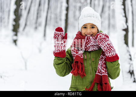 African American bambino in abiti caldi sorridente, salutando con la mano e guardando la fotocamera in winter park Foto Stock