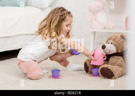 Adorable kid gioca con Teddy bear sul pavimento in camera per bambini Foto Stock